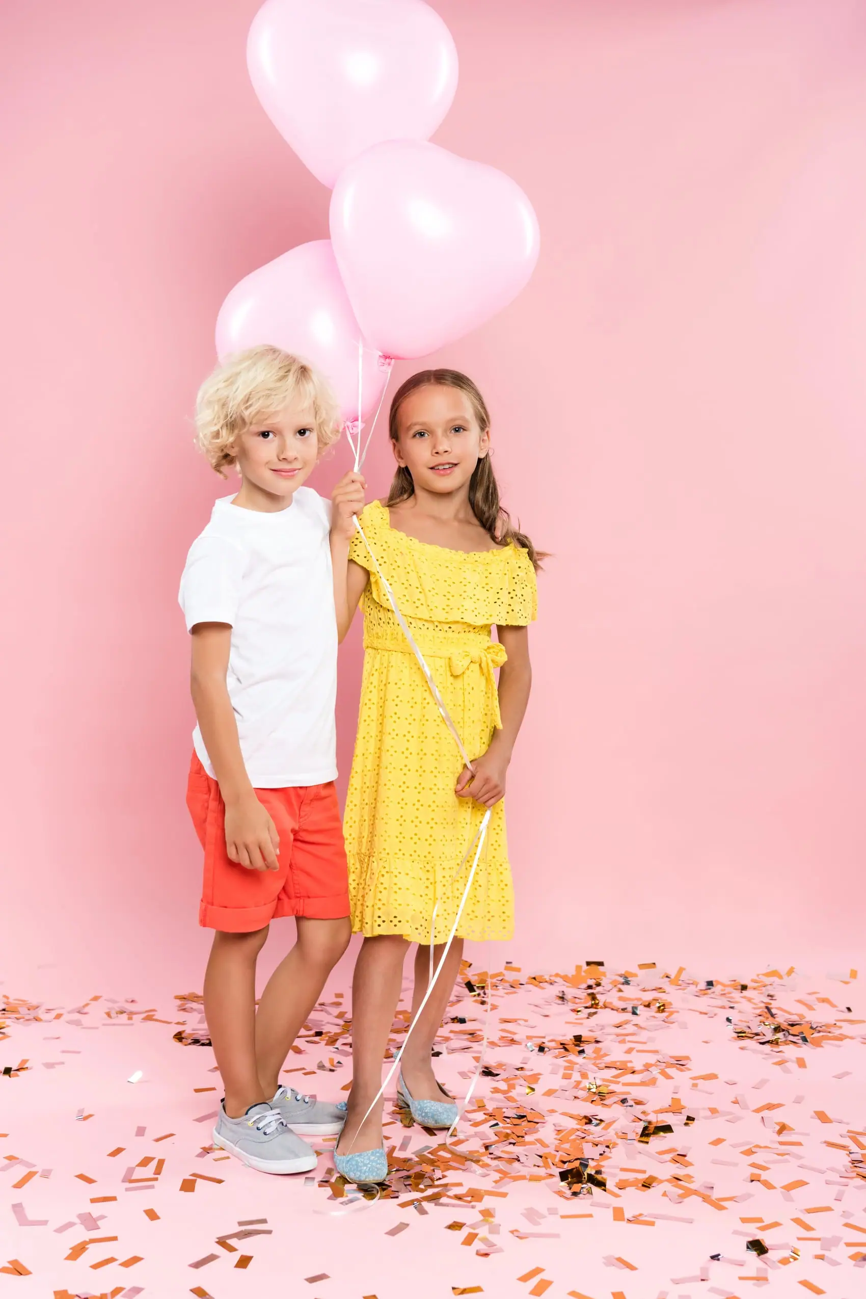 Mädchen und Junge mit rosa Herzluftballons feiern einen Kindergeburtstag